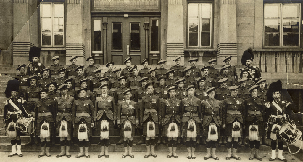 A vintage black and white group photograph showing a large military band or orchestra posed in formal uniforms in front of a building entrance.